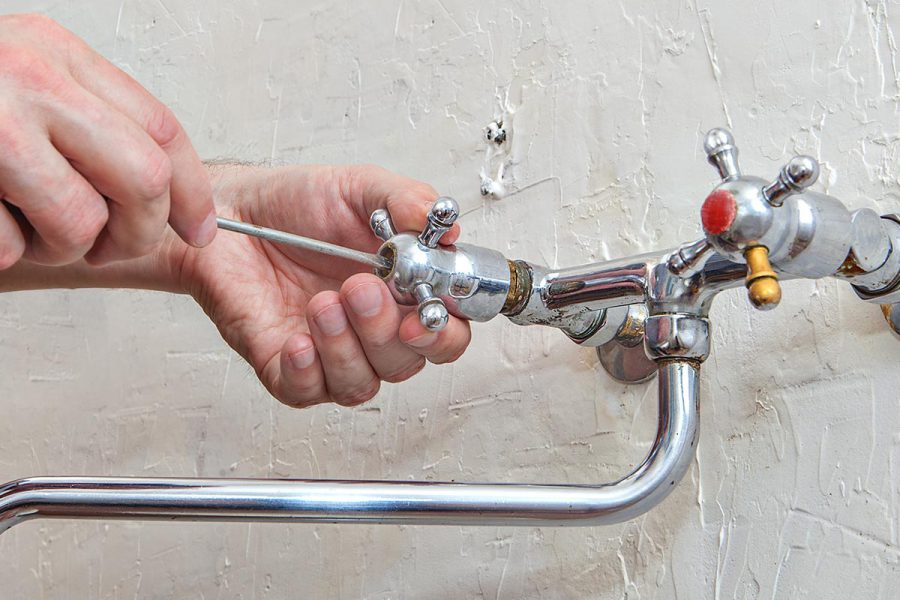 Plumbing repair, plumber unscrews handle kitchen faucet using hand screwdriver, close-up.